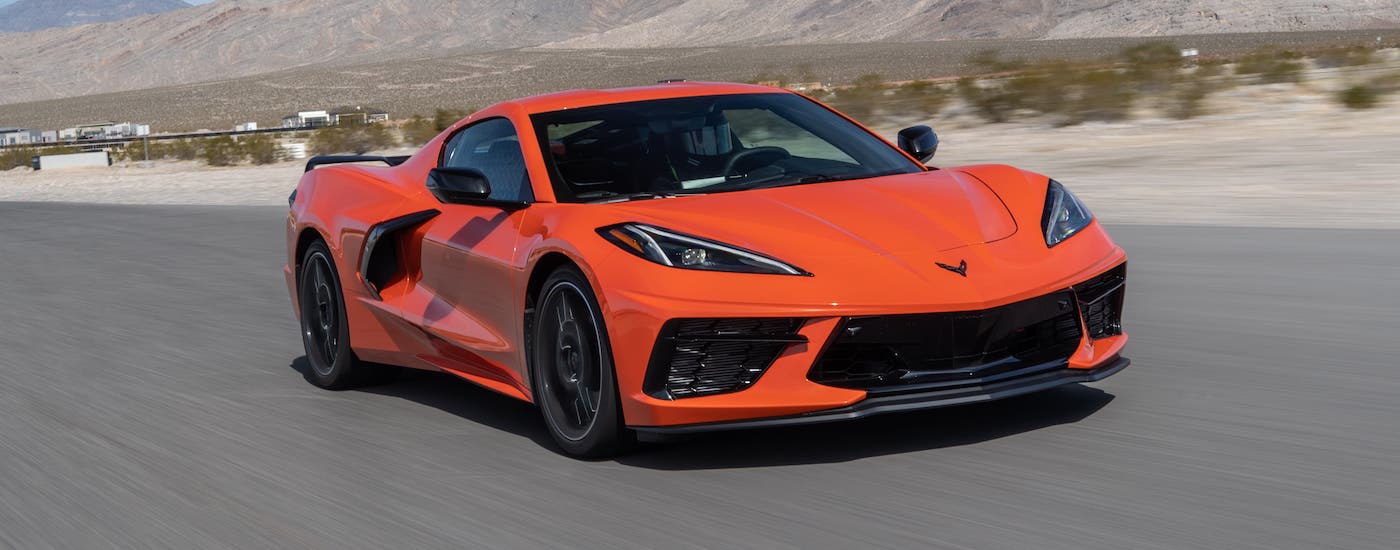 An orange 2020 Chevy Corvette Stingray is driving on an empty highway with mountains in the distance.