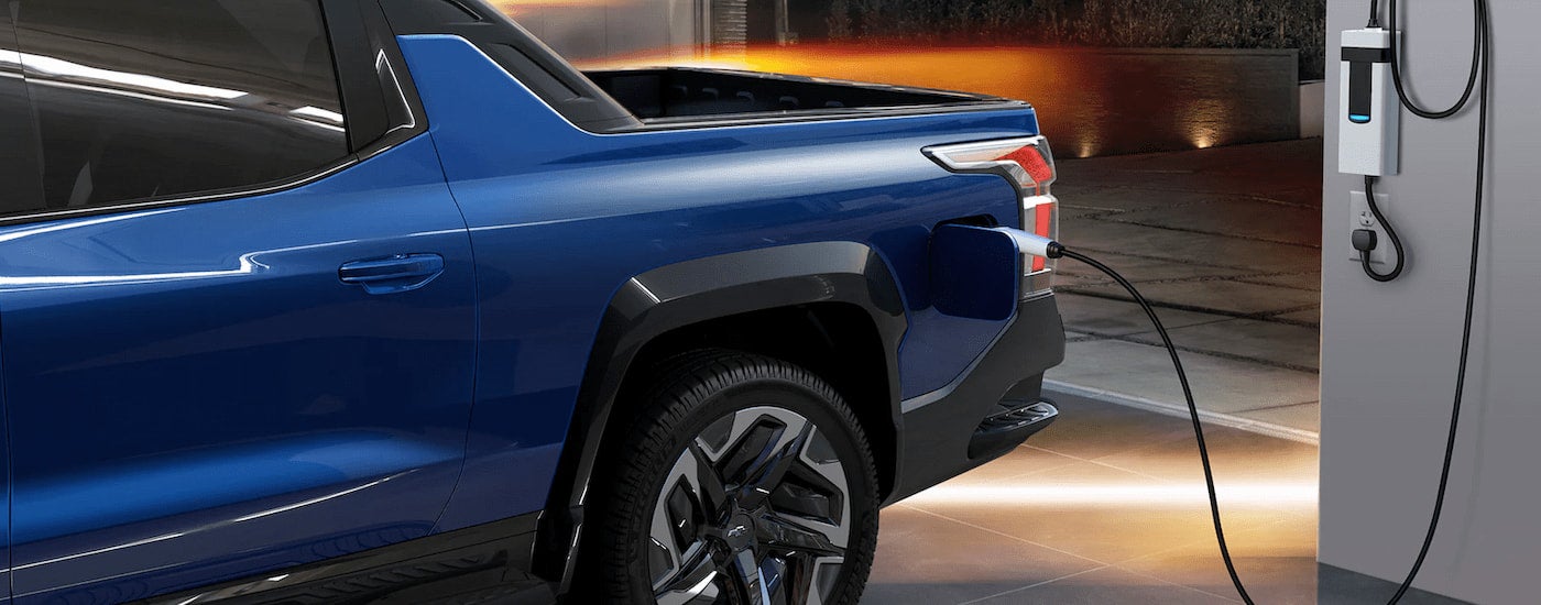 A blue 2024 Chevy Silverado 1500 EV is shown at a charging station.