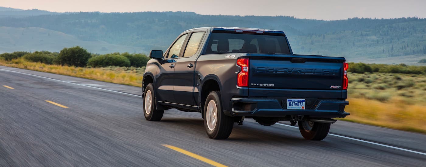 A blue 2021 Chevy Silverado 1500 RST is driving away on an empty highway.
