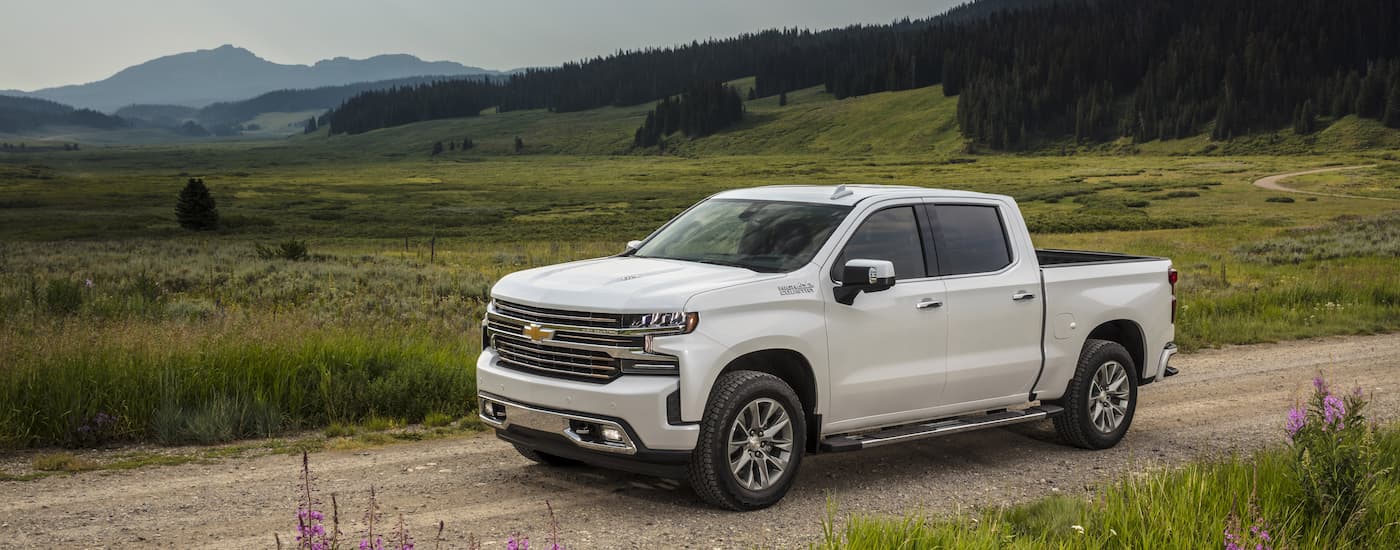 A white 2021 Chevy Silverado 1500 High Country is shown parked on a dirt road surrounded by grass.