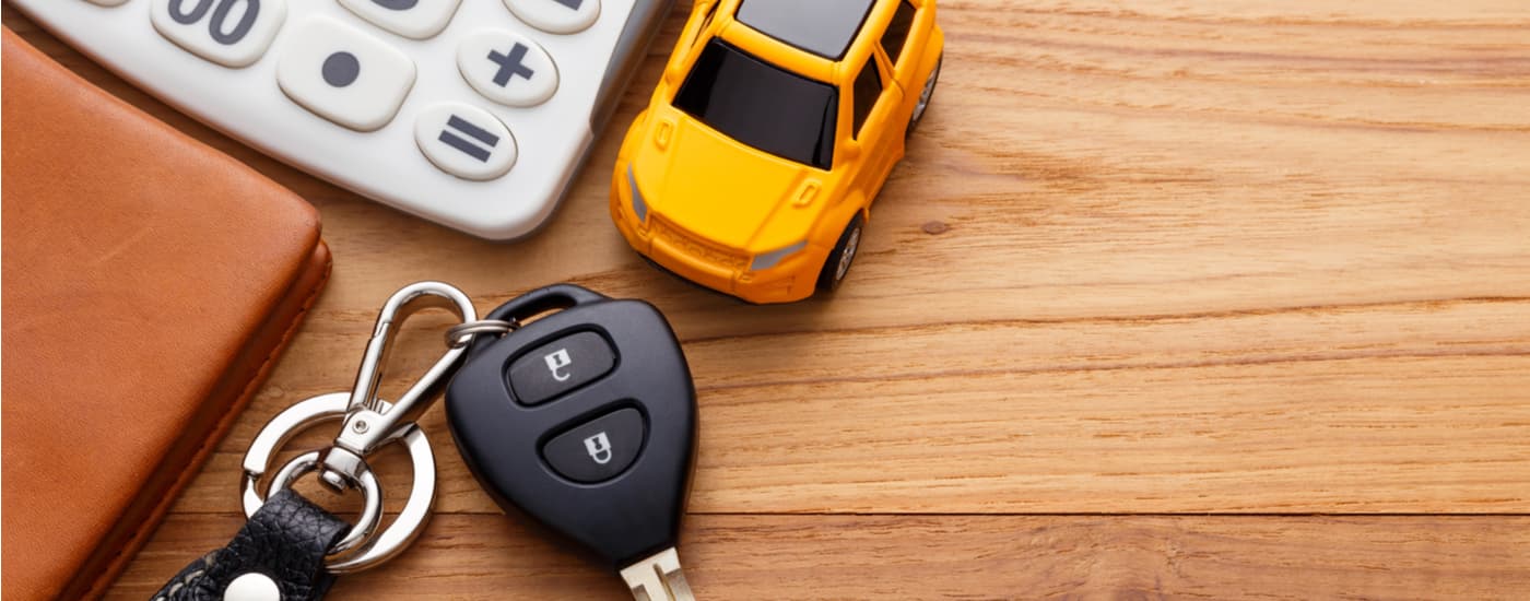 A yellow toy car is shown on a wood table next to a car key and calculator.