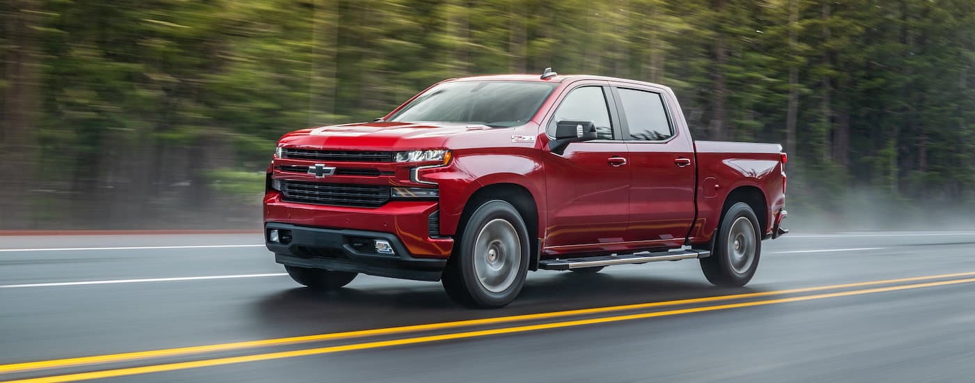 A red 2020 Chevy Silverado 1500 is shown driving on a tree-lined road.
