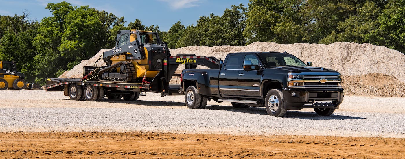 A black 2017 used Chevy Silverado 3500 is towing construction equipment at a gravel pit.