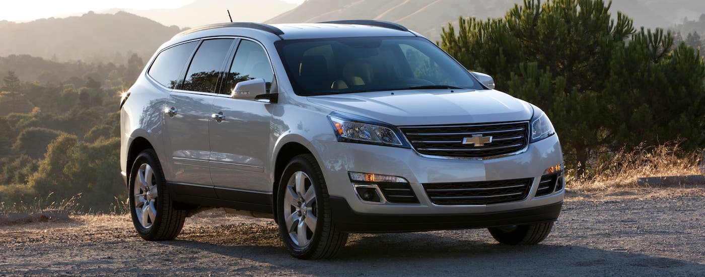 A silver 2015 used Chevy Traverse is parked in front of mountains at sunset.