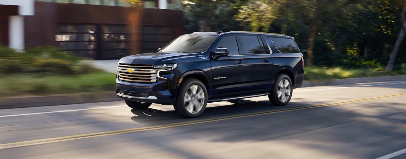 A blue 2021 used Chevy Suburban for sale is shown driving on a city street.