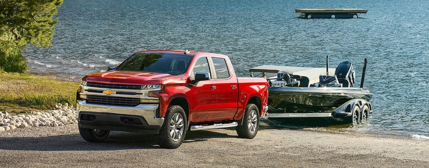 A red 2022 Chevy Silverado 1500 is shown towing a boat out of a lake.