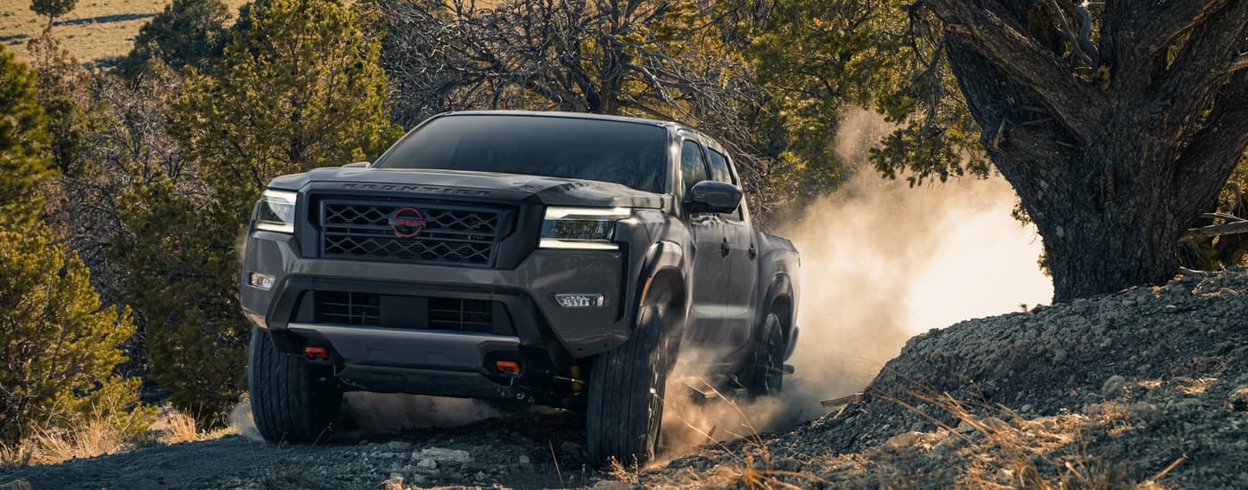 A grey 2023 Nissan Frontier PRO-4X is shown off-roading on a rocky trail.