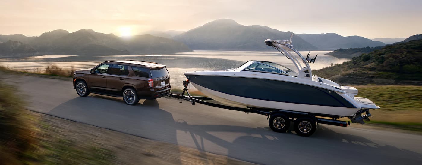 A brown 2022 Chevy Tahoe RST is shown from the side towing a boat next to a lake.