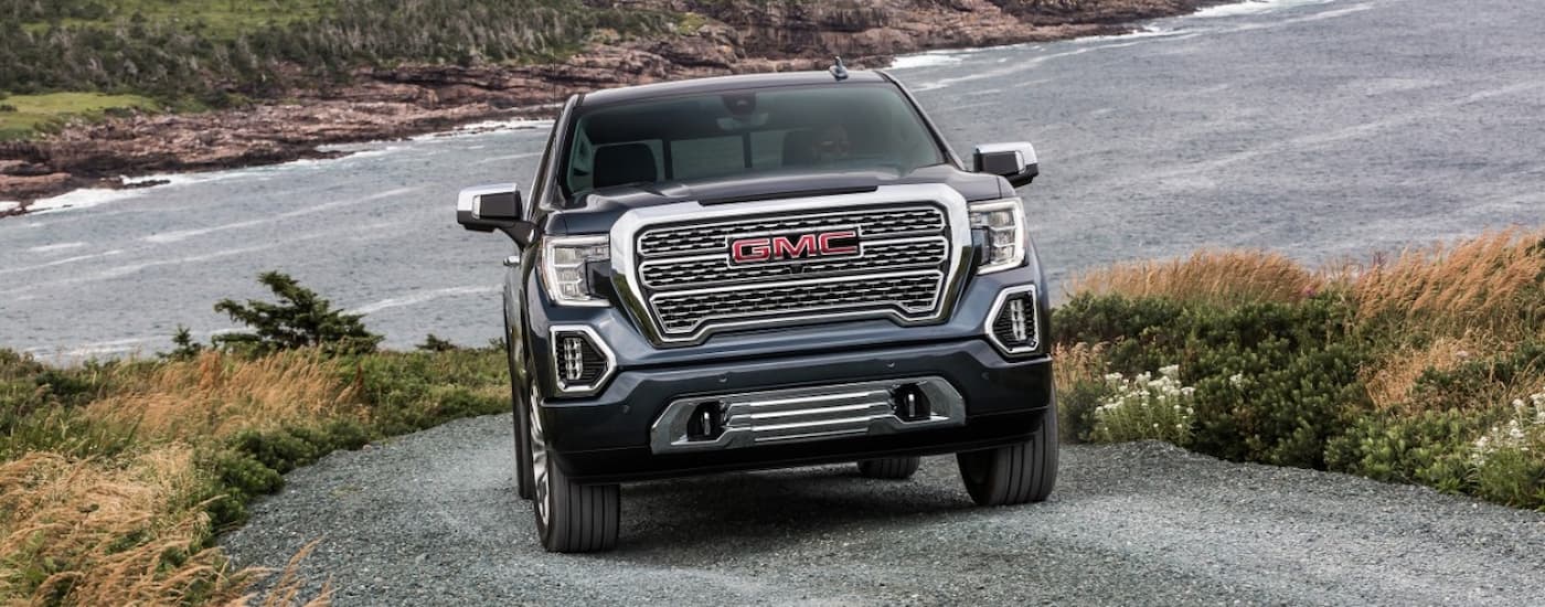 A blue 2020 GMC Sierra 1500 Denali is shown from the front driving on a gravel road.