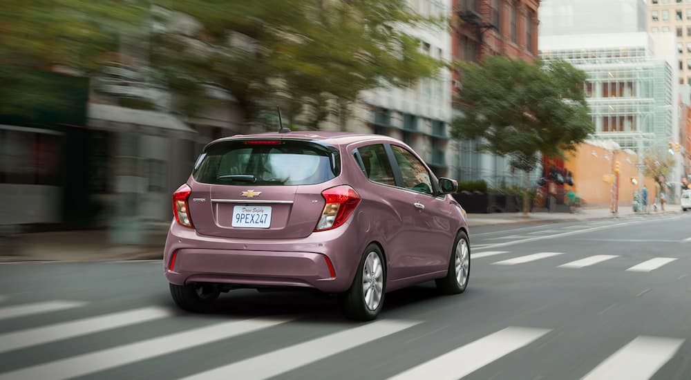 A pink 2021 Chevy Spark is driving on a city street.