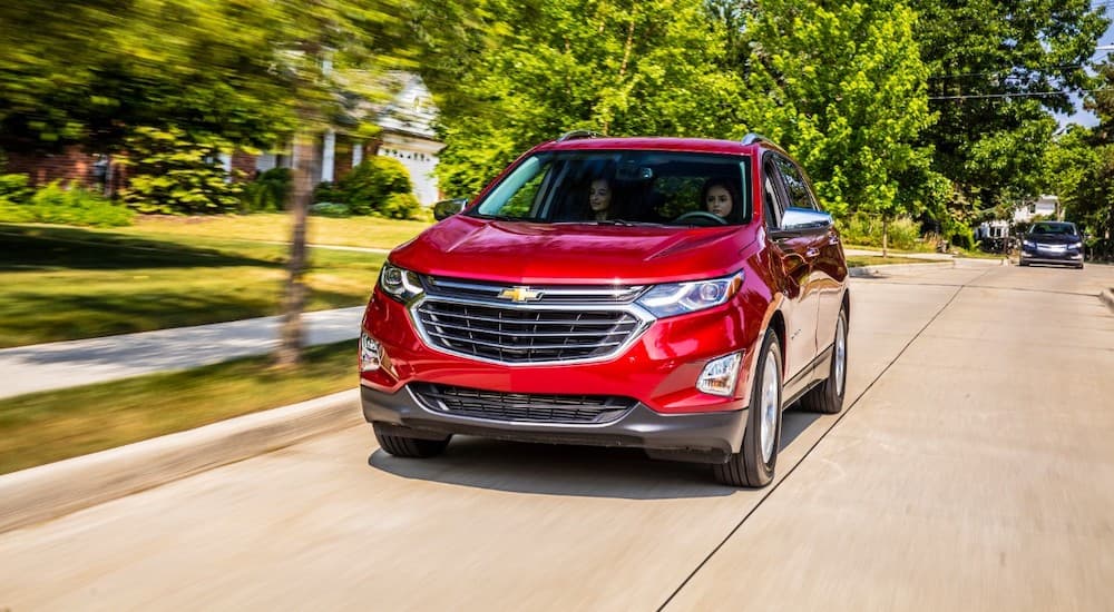 A red 2020 Chevy Equinox is driving on a neighborhood street.