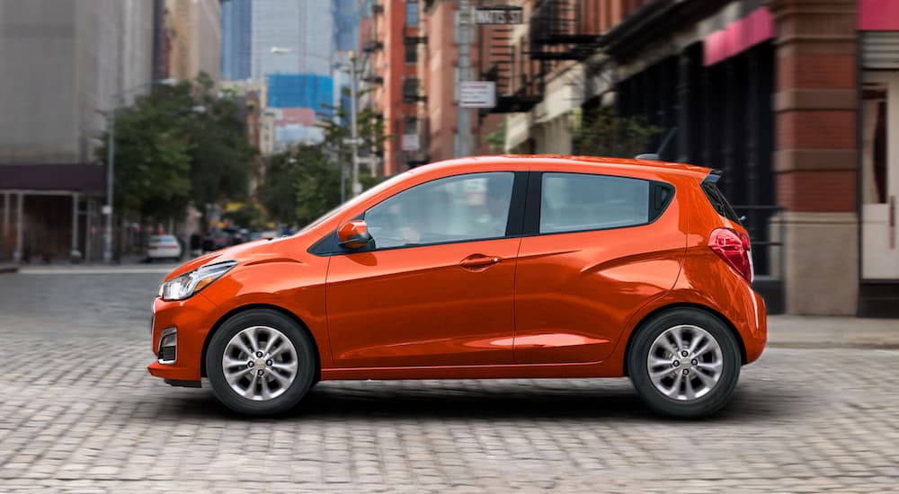 An orange 2021 Chevy Spark is shown from the side on a city street.