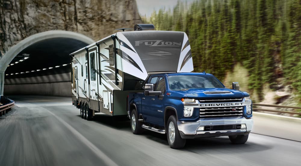 A blue 2021 Chevy Silverado 2500HD is towing a large camper out of a tunnel.