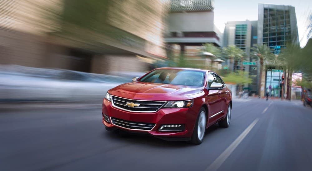 A red 2016 Chevy Impala is driving on a city street after leaving a used car dealer.