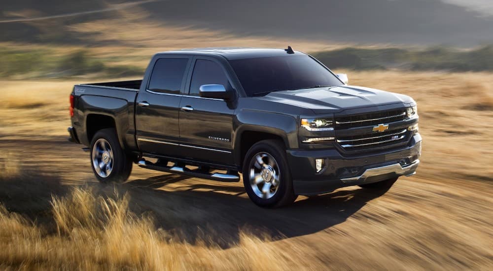 A black 2018 used Chevy Silverado is driving on a dirt road past a field.