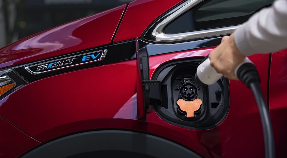 A closeup shows a red 2021 Chevy Bolt EV being charged.