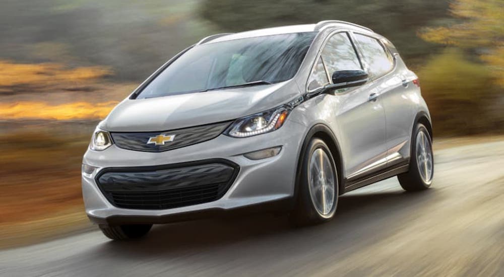 A silver 2021 Chevy Bolt EV is driving passed blurred trees after leaving a Chevy Dealer in Houston.