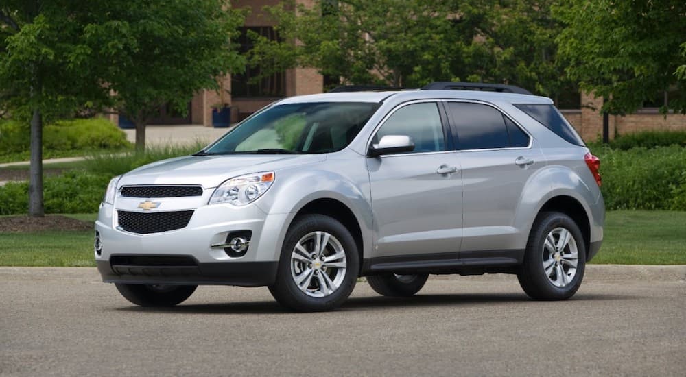 A silver 2009 used Chevy Equinox is parked in front of trees and a brick building.