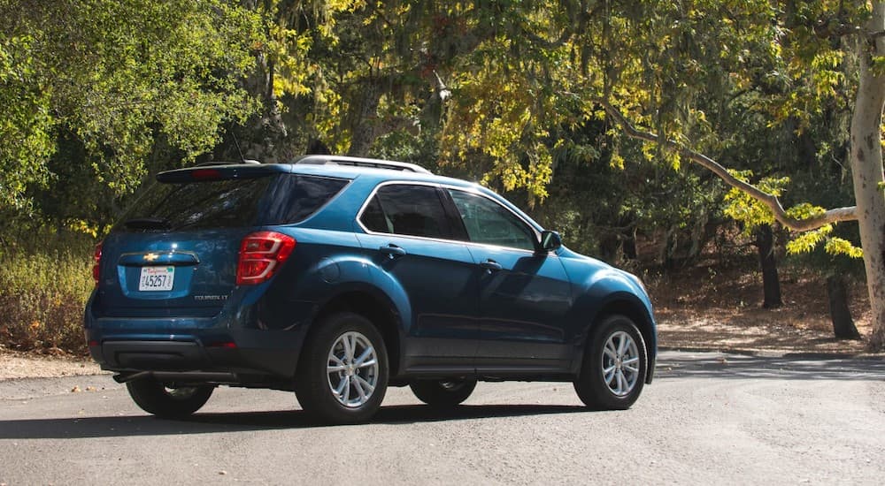 A blue 2016 used Chevy Equinox is shown from the rear while parked in front of trees.