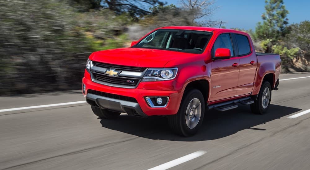 A red 2015 Chevy Colorado, a popular used Chevy truck in Houston, is driving on a highway past trees.