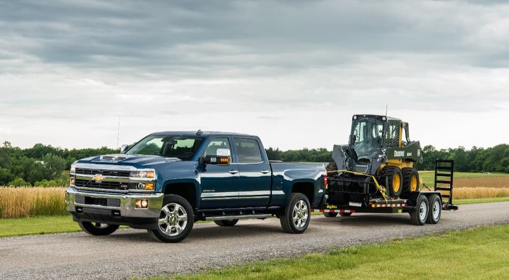 A blue 2018 Chevy Silverado 2500 is towing machinery past fields.