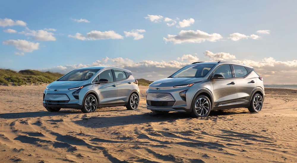 Two silver Chevy EVs, a 2022 Bolt and 2022 Bolt EUV, are parked on beach sand.