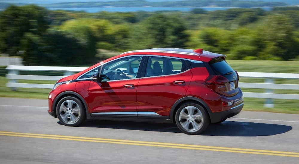 A red 2020 Chevy Bolt EV is driving past a white fence and trees.