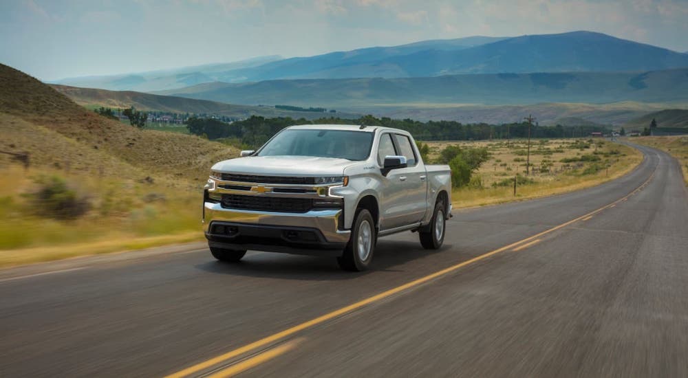 A silver 2020 Chevy Silverado LT is driving on a highway in front of mountains.
