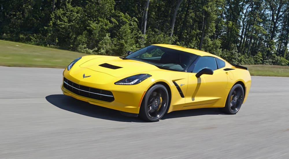 A popular vehicle at used Chevy dealers in Houston, a yellow 2014 Chevy Corvette, is shown driving down a wooded road.