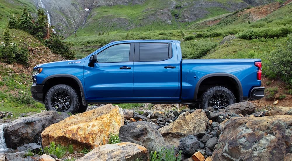 Popular at Houston Chevy truck dealers, a blue 2022 Chevy Silverado ZR2, is shown from the side parked near a grassy hillside.