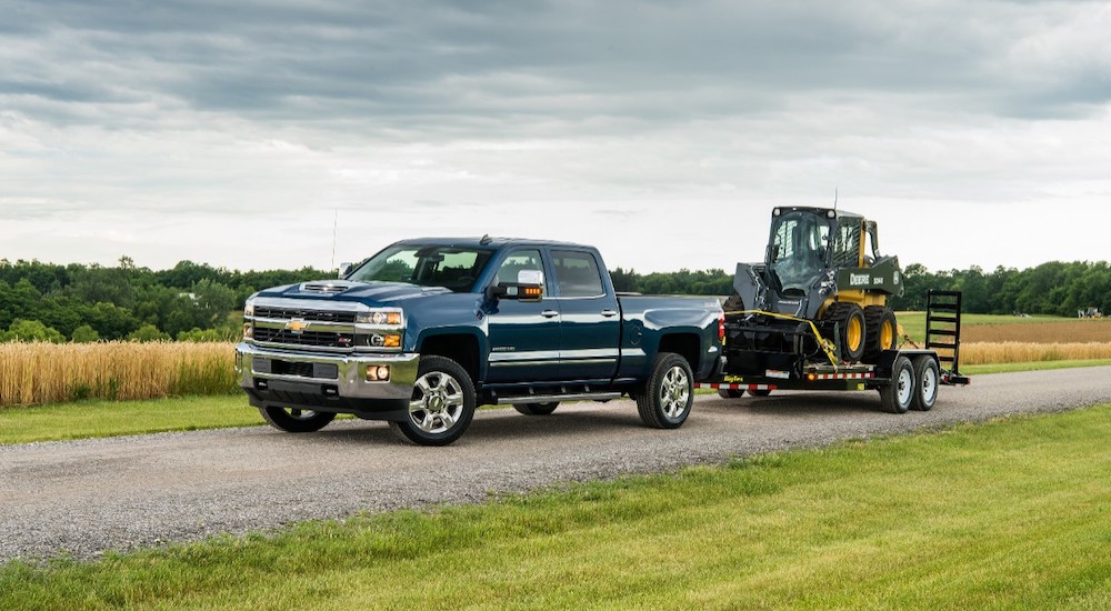 One of the most popular picks at a Houston used truck dealer, a 2018 Silverado 2500 HD is shown towing heavy machinery.