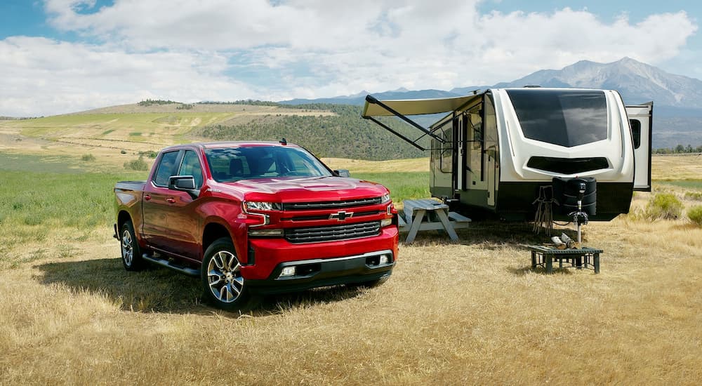 A red 2022 Chevy Silverado 1500 RST LTD is shown parked next to a camper in a field.