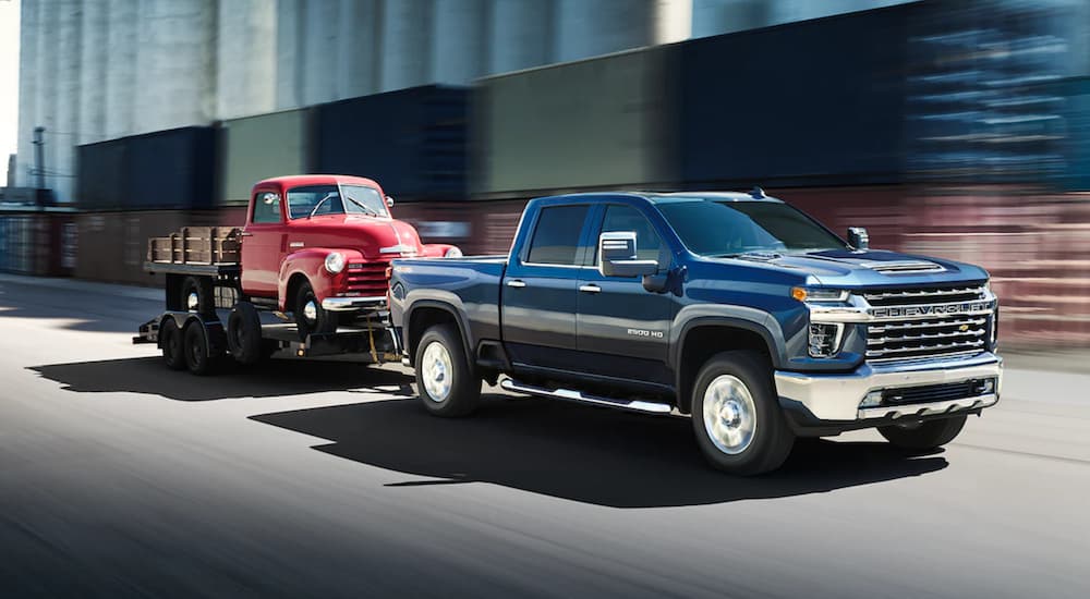 A blue 2022 Chevy Silverado 2500 HD is shown towing a vintage car after leaving a Conroe Chevy dealer.