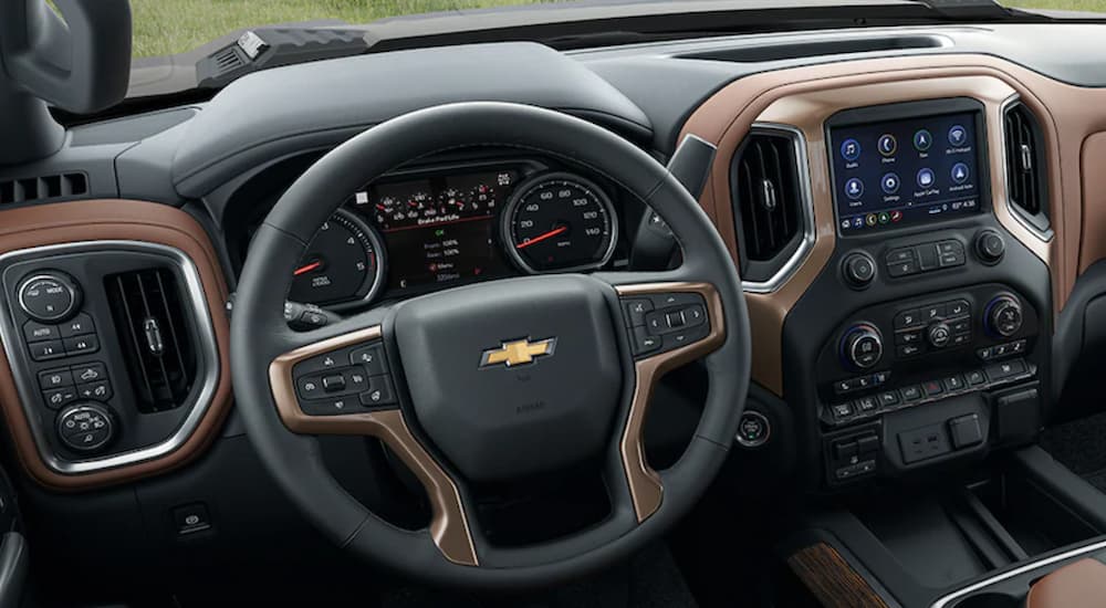 The black and brown interior of a 2022 Chevy Silverado 2500 HD shows the steering wheel and infotainment screen.