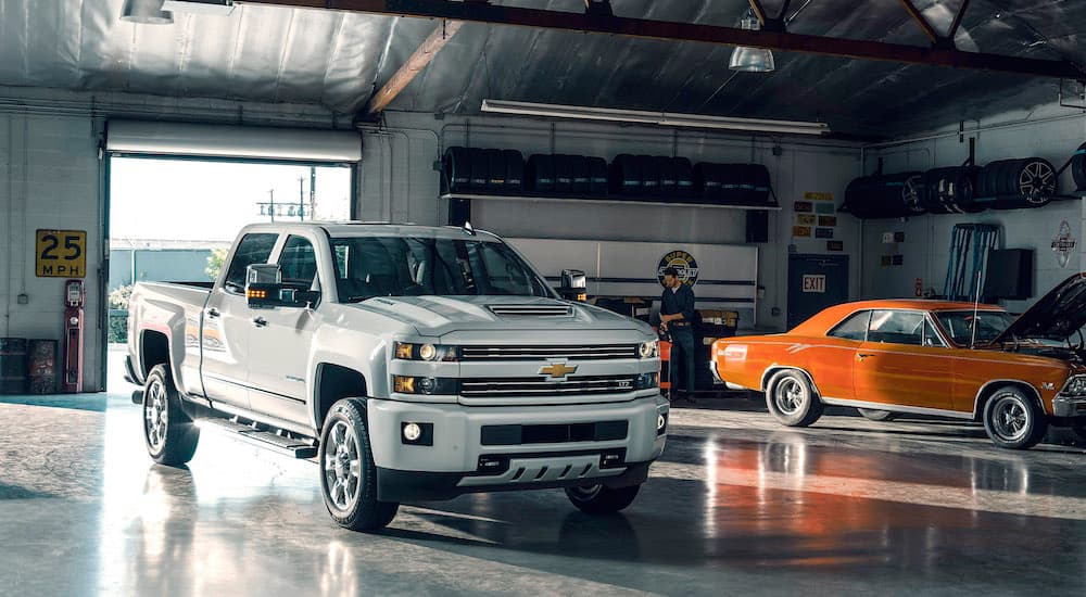 A white 2017 used Chevy Silverado 2500 HD LTZ is shown in a garage next to an orange muscle car.
