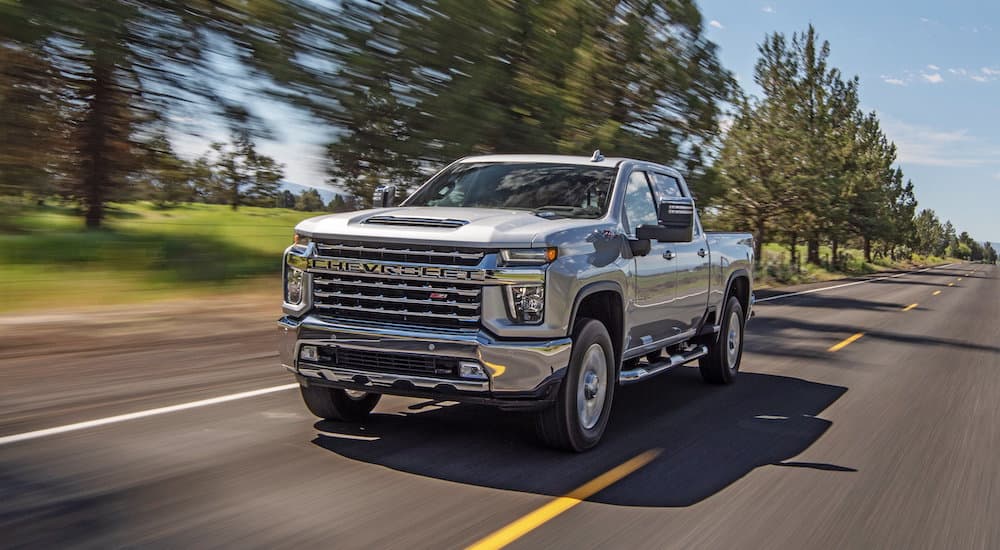 A silver 2021 Chevy Silverado 2500 HD Z71 is shown driving down a tree-lined road.