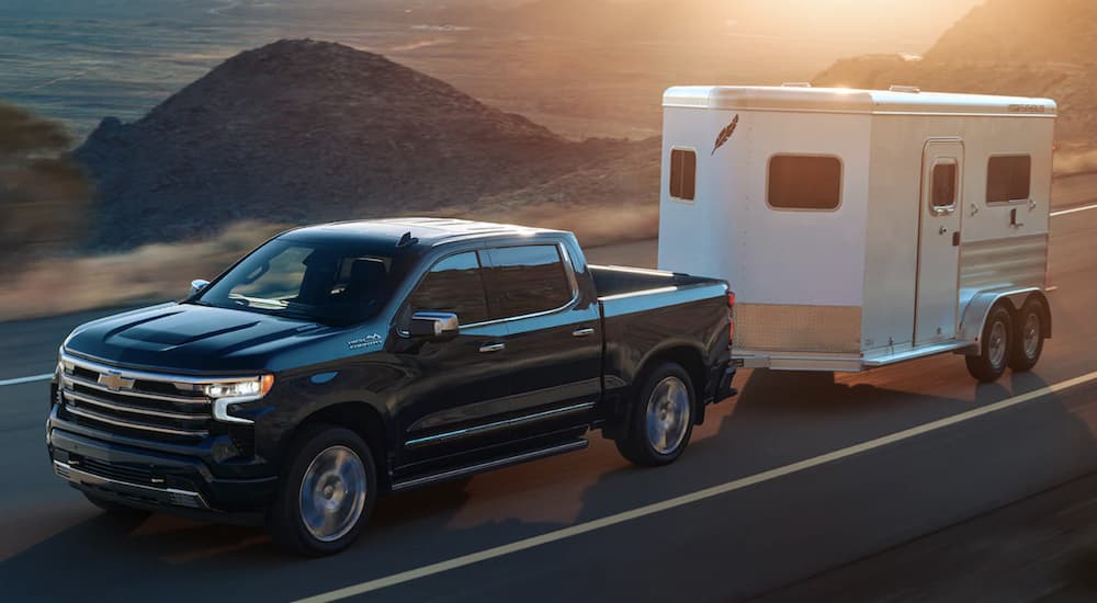 A black 2022 Chevy Silverado 1500 is shown from the side towing a white closed trailer on an open road.
