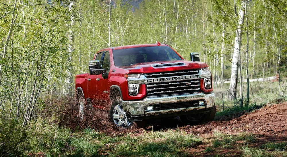 A red 2022 Chevy Silverado 2500HD is shown off-roading through a forest.