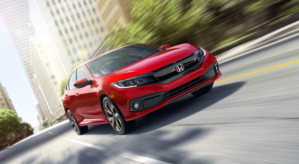 A red 2019 Honda Civic is shown from the front driving through a city after leaving a used car dealer.