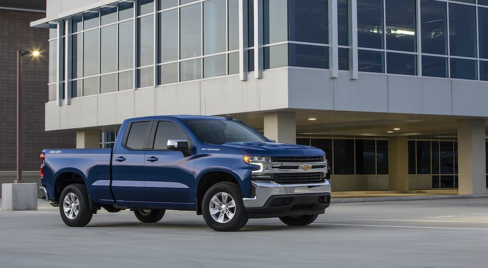 A blue 2019 Chevy Silverado 1500 is shown from the side parked in front of a pre-owned Silverado dealer.