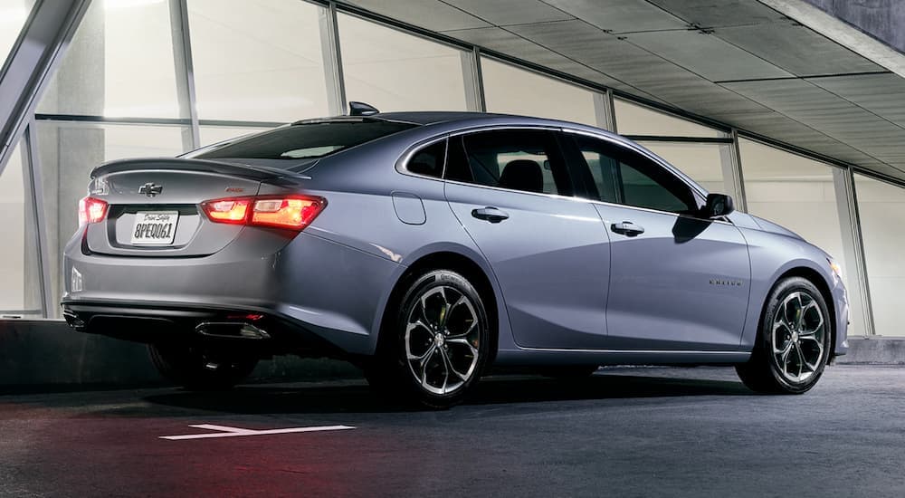 A silver 2019 Chevy Malibu is shown from the rear parked next to a building after visiting a used car dealer.