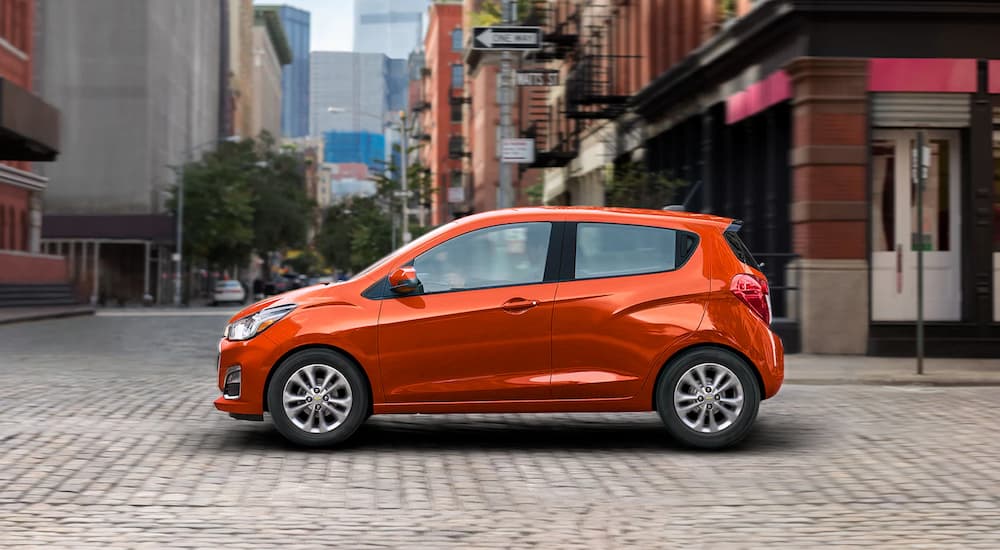 An orange 2021 used Chevrolet Spark is shown from the side driving on a city street.