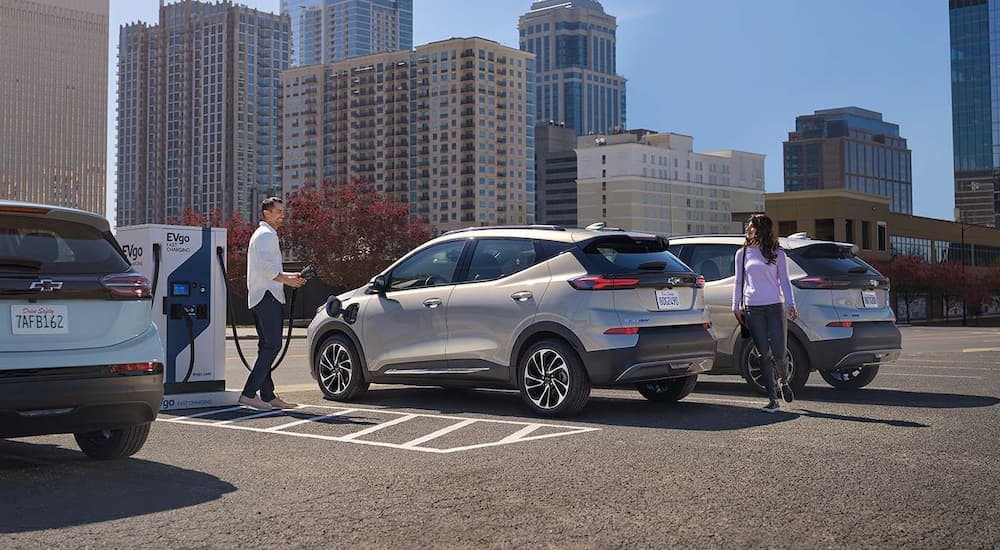 Three silver 2023 Chevy Bolt EVs are shown parked at charging stations. 