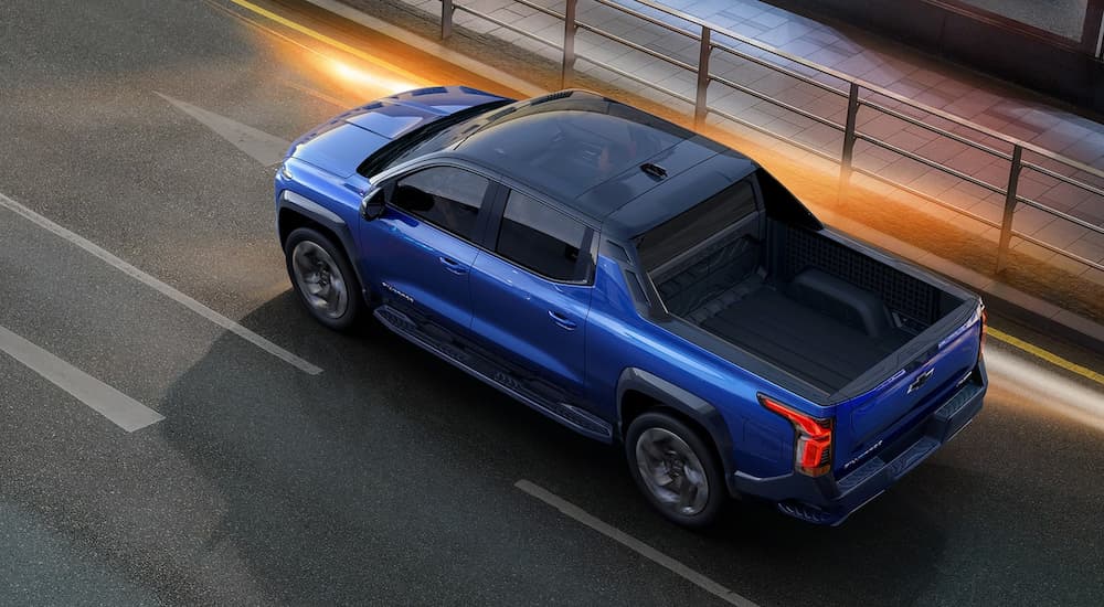 A blue 2024 Silverado EV is shown from a high angle driving on a city bridge.