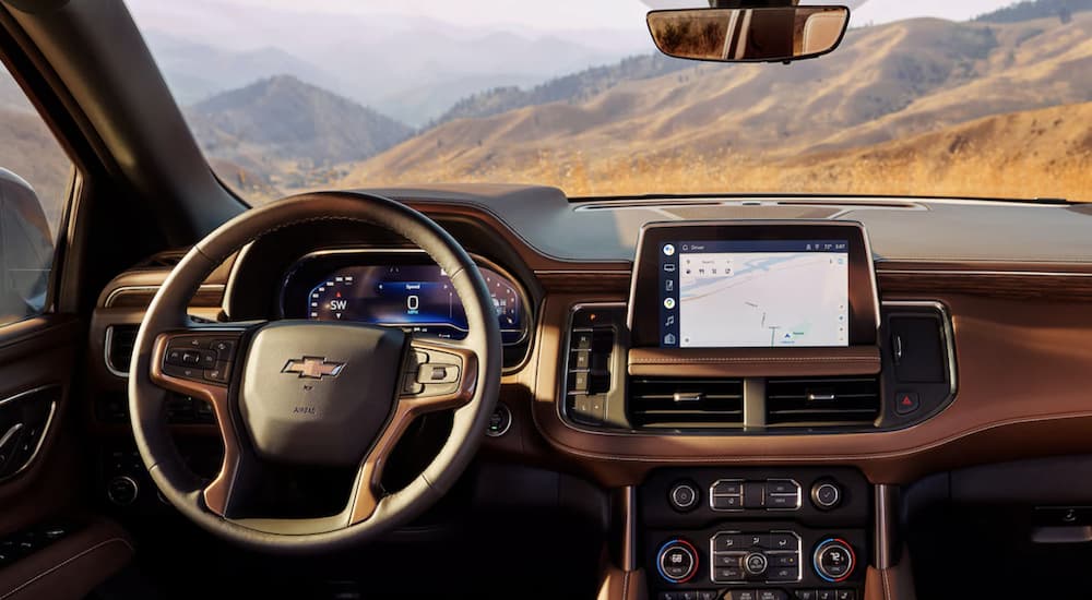 The brown interior of a 2023 Chevy Tahoe shows the steering wheel and infotainment screen.