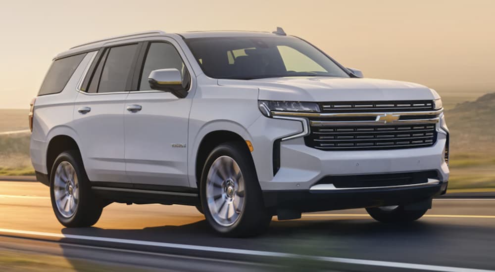 A white 2023 Chevy Tahoe is shown from the side driving on an open road.