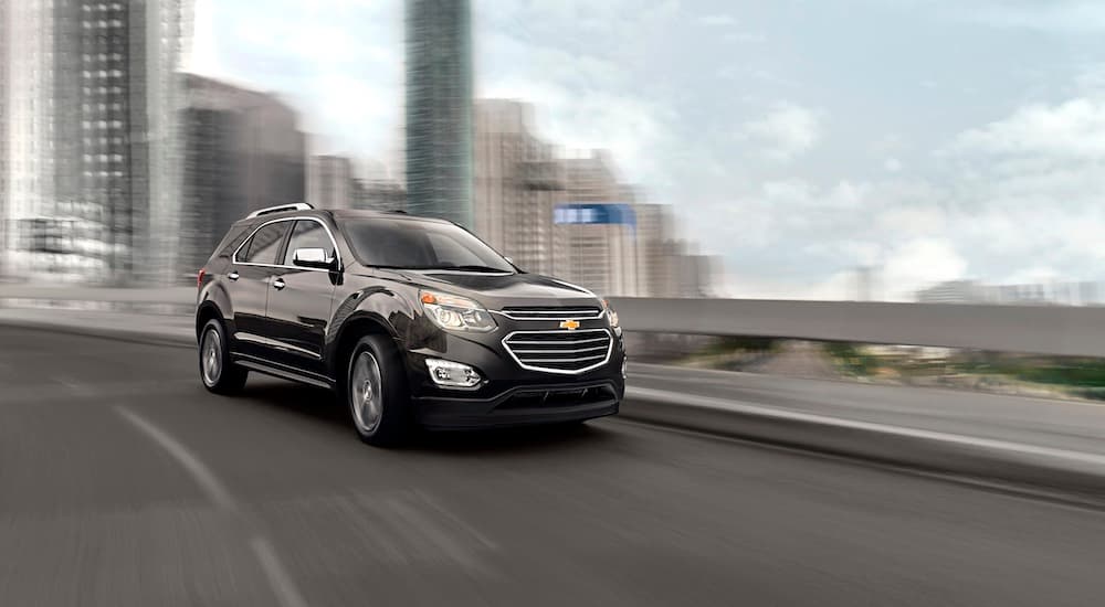 A grey 2016 used Chevy Equinox is shown driving past a blurred city.