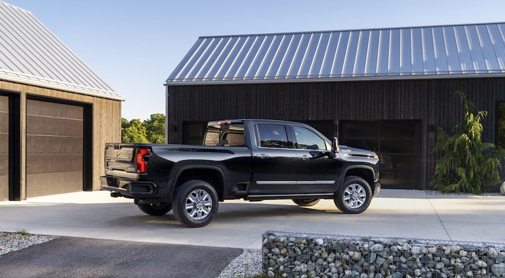 A black 2024 Chevy Silverado 2500 HD High Country is shown from the side while parked in a driveway after leaving a dealer that has a Chevy Silverado 2500 for sale.