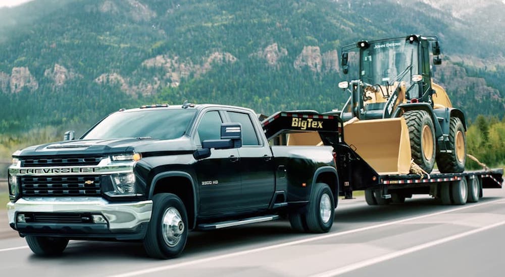 A black 2020 Chevy Silverado 3500 HD is shown from the front at an angle while towing a loader after leaving a dealer that has a used Chevy Silverado for sale.