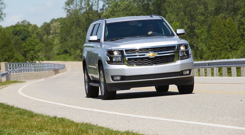 A popular used Chevy Tahoe for sale, a silver 2015 Chevy Tahoe LT, is shown driving on a highway.